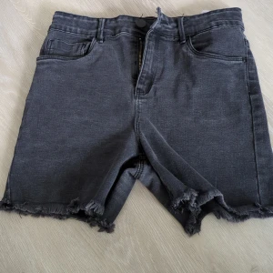 Svarta jeansshorts från LMTD - Svarta jeansshorts från LMTD med råa, fransiga benslut och klassisk femficksdesign. Shortsen har hög midja och dragkedja framtill. Perfekta för en chill och trendig look under sommaren.