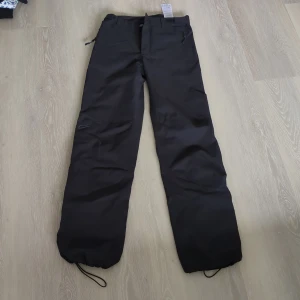 Svarta överdragbyxor från Five Seasons - Svarta överdragbyxor från Five Seasons med justerbar midja, dragkedjeförsedda fickor och dragsko vid benslut. Perfekta för kalla dagar med sitt slitstarka yttertyg och meshfoder. Snygg och funktionell design för vinterns alla äventyr.