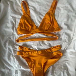 Orange bikini med snygga band från H&M - Superfräsch orange bikini från H&M med coola banddetaljer både på överdelen och trosan. Bikinin har breda axelband, triangelformad topp och extra band som korsas under bysten och på höfterna. Perfekt för stranden eller poolen i sommar! ÖVERDELEN ÄR I STORLEK 44 OCH UNDERDELEN I STORLEK 38