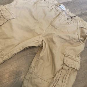 Beige cargoshorts från 157, medium - Snygga beige cargoshorts från 157 i storlek medium. Klassisk modell med flera stora fickor på sidorna och knappstängning i midjan. Perfekta för chill dagar eller när du vill ha en avslappnad stil. Gjorda i mjuk bomull för skön känsla hela dagen.