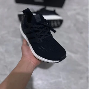 Adidas Ultraboost 4.0 svarta sneakers - Svarta Adidas Ultraboost sneakers med vit, tjock och dämpad sula. Ovandelen är i ventilerande syntetmaterial med klassiska tre ränder på sidan och snörning framtill. Perfekta för dig som vill ha både stil och komfort i vardagen. Med kvitto och box
