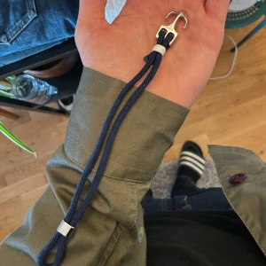 Blått armband med silverfärgad krok - Snyggt armband med marinblått band och en unik silverfärgad krok som lås. Bandet är gjort av slitstark textil och har en enkel men cool design, perfekt för dig som gillar stilrena accessoarer med en twist.