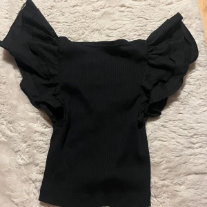 Svart Zara topp - Svart croppad topp från Zara med breda volangärmar och djup v-ringning.  Har haft på mig den en gång, den är helt ny!. 