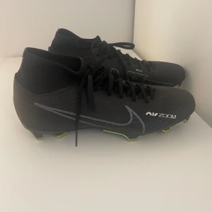 Nike Air Zoom svarta fotbollsskor - Snygga svarta Nike Air Zoom fotbollsskor med grå Swoosh och detaljer. Skorna har snörning, högre skaft och plös samt sulor med limegröna dobbar för bra grepp på planen. Tillverkade i syntetmaterial för lätt känsla och snabbhet. Använda 2 gånger. Sänker priset vid snabb affär
