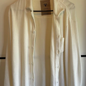 Vit frottéskjorta från OAS - Snygg vit skjorta från OAS i mjuk frotté. Skjortan har klassisk krage, knäppning framtill och långa ärmar. Perfekt för en chill och avslappnad stil, lätt att matcha med både shorts och jeans. Helt oanvänd inprincip ny! Ny pris runt 1500kr