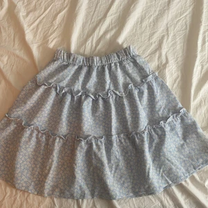 Blommig volangkjol från H&M ljusblå - Supersöt ljusblå kortkjol från H&M med vita små blommor och volangdetaljer. Kjolen har resår i midjan och är perfekt för dig som gillar en romantisk och somrig stil. Lätt och luftig, passar perfekt till sneakers eller sandaler. Pris kan diskuteras