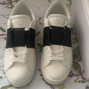Valentino Garavani Open sneakers vit/svart - Säljer ett par Valentino Garavani Open sneakers i vit skinn med bred svart läderdetalj över snörningen. Klassisk rund tå och platt sula, med subtila gulddetaljer på insidan. Kommer med originalpåse och box. Perfekt för dig som gillar stilrena designer. Jag har använt dom en gång dom är helt nya priset går att diskuteras  box dustbag kort äktenhet följer mer 