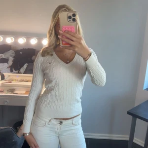 Vit kabelstickad v-ringad tröja - Säljer en vit kabelstickad tröja från GANT med v-ringning och lång ärm. Tröjan har en slim passform och diskret logga på bröstet. Perfekt att styla med jeans eller kjol för en clean look. Materialet är mjukt och stretchigt, vilket gör den skön att bära. Aldrig använt har bara legat i min garderob. Original pris 1600kr