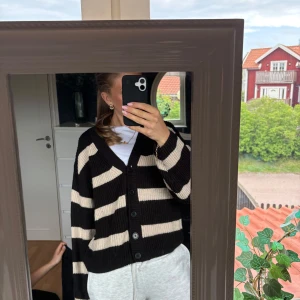 Randig svart och beige kofta - En supermysig höstig stickad kofta med breda svarta och beige ränder. Koftan har v-ringning, stora knappar framtill och långa ärmar. Bara att be om fler bilder!!