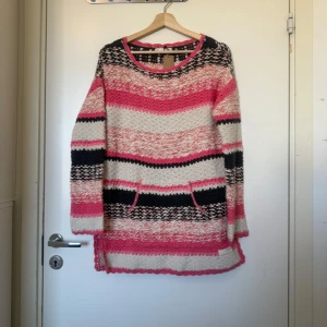 Randig stickad tröja i rosa och svart - Säljer en lång, randig stickad tröja från Odd Molly i färgerna rosa, svart och vit. Tröjan har rund hals, långa ärmar och två fickor framtill. Perfekt för dig som gillar färgglada och mysiga plagg med unik design. Storlek 1 som enligt deras storleksguide motsvarar en storlek S, men den är otroligt rymlig i storlek. Kanske mer en L/XL.  Mycket fint skick, jag hittar inga synliga anmärkningar eller defekter.
