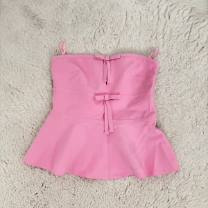  Topp med rosetter - Supersöt rosa bandeau topp från ZARA med två dekorativa rosetter framtill. Toppen har en utsvängd nederdel och är axelbandslös för en clean look. Perfekt för dig som vill sticka ut med en feminin och trendig vibe. Aldrig använd ❤️