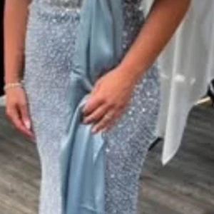 Lång glittrig ljusblå balklänning - Magisk långklänning i ljusblått med massor av glittrande paljetter över hela klänningen. Snygg figurnära passform och en elegant slits framtill. Klänningen har en vacker omlott-detalj och breda axelband. Perfekt för bal, fest eller bröllop. Köpt för 6900kr. Klänningen är insydd till storlek 36. Går att sprätta upp till ”orginal storlek” - strl 40. Använd endast ett fåtal timmar.  