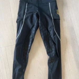 Svarta träningsleggings från Maya delorez  - Säljer ett par svarta Maya delorez leggings med guldigt logotryck på benet och reflekterande detaljer. Tight passform och stretchigt syntetmaterial, perfekt för träning. Snyggt mönster på insidan av benen för extra grepp och stil.