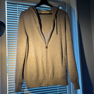 Grå kashmirhoodie från Sayless - Mjuk och lyxig grå hoodie från Sayless i kashmir. Tröjan har dragkedja framtill, huva med snörning och långa ärmar. Perfekt för dig som gillar en clean och chill stil med premiumkänsla. Snygg till jeans eller mjukisbyxor.