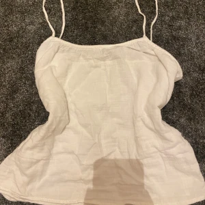 Vit linnetopp från H&M XS - Säljer en enkel och fräsch vit linnetopp från H&M i storlek XS. Toppen har tunna axelband och är tillverkad i ett luftigt linnematerial, perfekt för varma dagar. Stängs med en liten knapp i ryggen. Stilren och lätt att matcha med allt.
