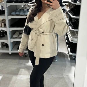 Beige trenchcoat med bälte - Snygg beige trenchcoat med bred krage, dubbelknäppning och knytskärp i midjan. Super fin till vardags och för att klä upp sig. 