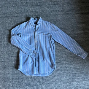 Ralph Lauren skjorta - Blå skjorta från Ralph Lauren med vita och ljusrosa ränder. Skick 9.5/10. Tvättad fåtal gånger. Hör av dig vid minsta fundering!