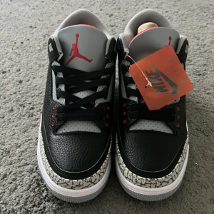 Nike Air Jordan 3 Black Cement EU41 - Nike Air Jordan 3 Black Cement med svart och grått skinn, ikoniskt elephant print och röda detaljer. Klassisk Jumpman-logga på plösen och Nike Air på hälen. Perforerad grå ovandel, svart snörning och vit/grå sula med röd detalj undertill. Perfekt för dig som vill sticka ut.