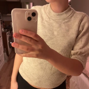 Beige stickad tröja med kort ärm - Supermysig beige stickad tröja med korta ärmar och rund hals. Tröjan har ribbade muddar vid ärmslut och nederkant, vilket ger en snygg och enkel look. Perfekt att matcha med jeans eller kjol för en chill stil.