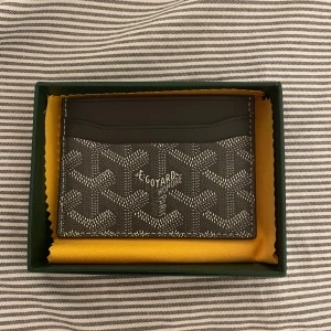Goy4rd plånbok  - Säljer en stilren mörk cardholder. Plånboken är i smidig modell med flera kortfack och präglad logga. Tillverkad i exklusivt skinn och levereras i original grön ask med gul tygpåse. Träffas i Stockholm och priset är ej hugget i sten. 