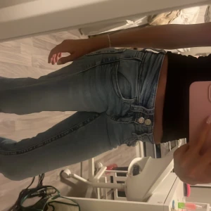 Ljusblå low Rise bootcut jeans med dubbla knappar - Säljer ett par ljusblå jeans med bootcut-modell och snygg tvätt. Jeansen har dubbla knappar i midjan och klassiska fickor fram och bak. De är högmidjade och har en lätt utsvängd passform nertill. Perfekta för dig som gillar retrovibbar och vill ha en cool look.