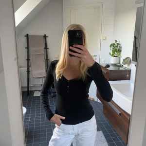 Svart ribbad långärmad topp - Svart långärmad topp med v-ringning och knappar framtill. Tröjan är ribbad och har en slim passform som sitter snyggt på kroppen. 