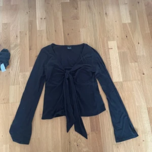 Svart långärmad omlottopp - Svart långärmad topp från Gina Tricot med v-ringning och snygg knytning framtill. Modellen är croppad och har lätt utsvängda ärmar. Perfekt för dig som gillar trendiga och stilrena plagg.