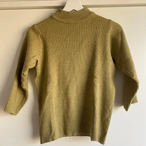 Olivgrön ribbad tröja - Olivgrön ribbstickad tröja med halvlånga armar. Köpt på IJ-Hallen i Amsterdam och dess då små defekter har jag lagat, vilket syns på bild 2 och 3. Syns knappt och den är väl duglig att använda! 