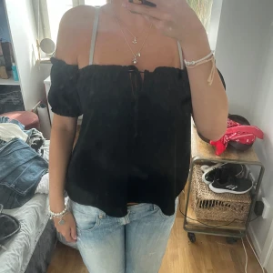 Svart offshoulder topp från Parisian - Säljer en svart offshoulder topp från Parisian med puffiga korta ärmar och söt snörning framtill. Toppen har en lätt rynkad kant upptill och är luftig i modellen, perfekt för varma dagar. Enkel att styla med jeans eller kjol.