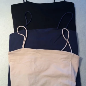 3-pack linne toppar Gina Tricot - Tre stilrena linne toppar från Gina Tricot i svart, marinblå och ljusrosa. Alla har smala axelband och croppad passform, perfekta till jeans eller kjol. Mjukt bomullsmaterial som känns skönt mot huden. Säljes som paket!