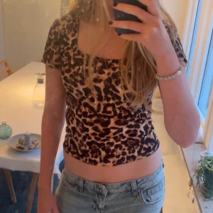 Leopardmönstrad topp från JDY - Säljer en croppad topp från JDY med leopardmönster i bruna och svarta toner. Toppen har korta ärmar, fyrkantig ringning och är figurnära i modellen. Perfekt för dig som vill sticka ut med ett djurmönstrat plagg.
