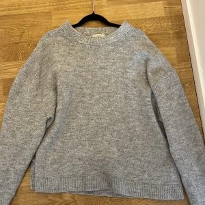 Grå stickad tröja från Gina Tricot - Mysig grå stickad tröja från Gina Tricot med rund halsringning och ribbade muddar. Tröjan har en relaxed passform och är perfekt för lager-på-lager. Enkel och stilren design som funkar till allt. Materialet är mjukt och skönt mot huden. Storlek L