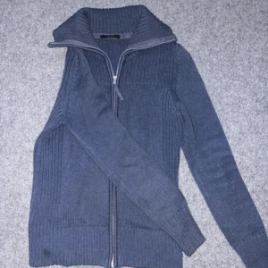 Blå ribbstickad kofta med dragkedja - Mysig blå ribbstickad kofta från H&M med hög krage och hel dragkedja framtill. Tröjan är långärmad och har en klassisk, stilren look som passar perfekt till jeans eller kjol. Materialet är bomull och polyamid för en skön känsla.