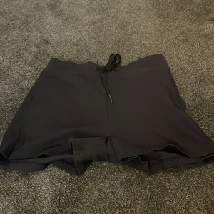 Svarta sportshorts Filippa K S - Svarta sportiga shorts från Filippa K Soft Sport i storlek S. De har elastisk midja med snörning och är tillverkade i ett mjukt, lätt material som passar perfekt för träning eller chill. Klassisk loose fit och stilren design.