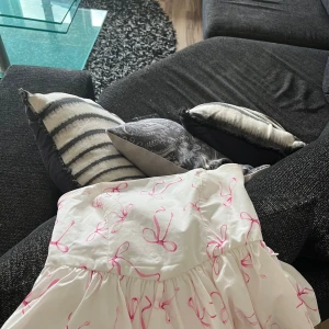 Vit tub topp med rosa rosetter - Supersöt vit  tub topp från FB Sister med rosa rosett-mönster. Axelbandslös modell med smock i ryggen för en bekväm passform. Perfekt för dig som vill ha en lekfull och feminin look. Tillverkad i ett lätt och skönt material.