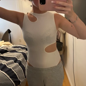 Vit ribbad cut out body - Säljer en vit ribbad body med coola cut out-detaljer vid axel och midja. Toppen är ärmlös och har en tight passform som framhäver figuren. Perfekt för dig som vill sticka ut med en trendig och edgy look.