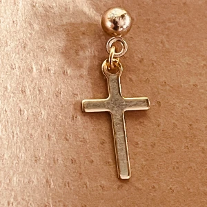 By prisförslag- 1 st Klassisk korsörhänge i guldton - Snyggt örhänge med ett stilrent kors i guldton, hängande från en rund kula. Korset har en enkel och modern design som passar dig som gillar minimalistiska smycken med lite edge. Perfekt att matcha med andra örhängen eller bära solo för en clean look.