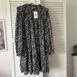 Leopardmönstrad klänning Pernilla Wahlgren - Snygg klänning från Pernilla Wahlgren Design i storlek L eller 44/46 (passar både L och XL). Klänningen har ett coolt leopardmönster i svart och beige, med volangdetaljer vid axlarna och långa ärmar. Aldrig använd och har alla lappar kvar.