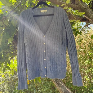 Blå kabelstickad kofta Odd Molly - Snygg blå kabelstickad kofta från Odd Molly med v-ringning och guldfärgade knappar framtill. Långärmad modell med ribbade muddar och nederkant. Perfekt att slänga över en t-shirt för en chill look. Diskret broderad detalj bak i nacken. Storlek 3 som enligt deras storleksguide motsvarar en storlek L. Fint skick, men den är tyvärr något tvättpåverkad. 