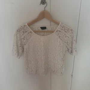 Vit spetsblus från Topshop - Superfin vit blus från Topshop i genombruten spets med korta ärmar och croppad passform. Perfekt att styla över ett linne eller bralette för en cool och romantisk look. Blusen har rund halsringning och är lätt transparent.
