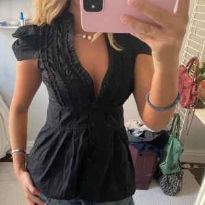 Svart blus med puffärm och knappar - Säljer denna supersnygga toppen köpt på Plick, (lånad bild) den är invikt på bilden och jag har den likadant då den är lite lång för mitt omtycke🫶 