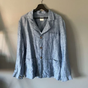 Blå linneskjorta från John Henric - Snygg blå skjorta från John Henric i luftigt linne. Klassisk krage, tre framfickor och knappar i brunt. Perfekt för dig som gillar en chill och stilren look. Långärmad modell med avslappnad passform och diskret struktur i tyget.