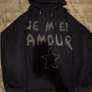 Mörk blå hoodie med glittertext - Text: 'JE M'EN AMOUR' mef en stjärna på framsidan.