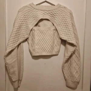 Beige croppad stickad linne och  bolero - Stickad linne och tillhörande bolero med snygga flätstickade detaljer. Perfekt för dig som gillar unika plagg med cool design och vill sticka ut lite extra.                                                                                 Boleron är använd vid ett tillfälle medan linnet är helt nytt.