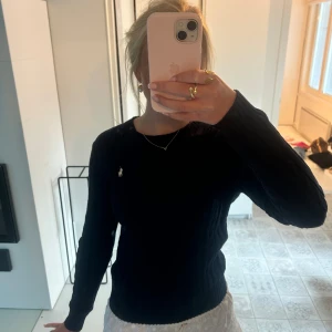 Mörkblå stickad tröja från Ralph Lauren - Oanvänd kabelstickad mörkblå tröja från Ralph Lauren med klassisk rund halsringning och vit broderad logga på bröstet. Tröjan har lång ärm och ribbade muddar, perfekt för lager-på-lager och snygg till både jeans och kjol. 