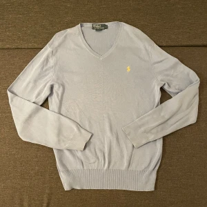 Ljusblå v-ringad tröja Polo Ralph Lauren - Snygg ljusblå v-ringad tröja från Polo Ralph Lauren i slim fit. Tröjan har lång ärm och klassisk gul broderad logga på bröstet. Tillverkad i mjuk bomull med ribbade muddar vid ärmslut och nederkant. Perfekt för dig som gillar stilrena och tidlösa plagg.