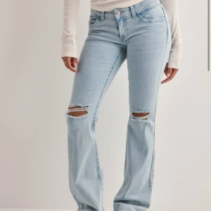 LOW waist bootcut jeans  - Säljer ett par ljusblå jeans med bootcut passform och slitna detaljer vid knäna. Baksidan har coolt rött broderi på fickorna som ger extra edge. Jeansen har klassisk femficksdesign och är tillverkade i denim.🥰De är uppsydda så de ska passa mig som är 164