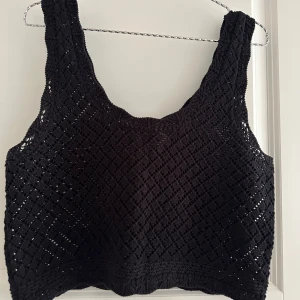 Svart virkad linnetopp från H&M Divided - Svart virkad linnetopp från H&M Divided i storlek M. Toppen har ett snyggt hålmönster och breda axelband. Perfekt för sommaren och enkel att styla med både jeans och kjol. Luftig och trendig look!