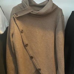 Beige kofta med knappar - Säljer en beige stickad kofta i storlek XL med unik omlottknäppning och stora knappar längs med. Koftan har långärmad design och en bred, mysig krage som ger extra stilpoäng. Perfekt för dig som gillar en chill och snygg look. Storlek XL. Mysig för både sommar och vinter.