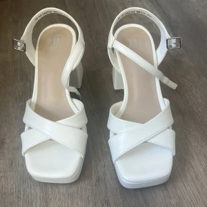 Vita chunky sandaler med klack från XIT - Snygga vita sandaler från XIT med breda korsade remmar och justerbart spänne runt ankeln. Skorna har fyrkantig tå, hög blockklack och plattform för extra attityd. Tillverkade i syntetmaterial med stilren look, perfekta för dig som gillar statement-skor. Använda 1 gång på skolavslutningen. Ny pris är 500 men säljer för 300, pris kan diskuteras